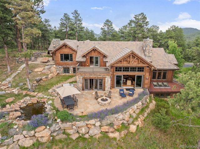 2929 Highlands View Rd, Evergreen, CO 80439 - back of house with a patio area, board and batten siding, stone siding, an outdoor living space with a fire pit, and a chimney