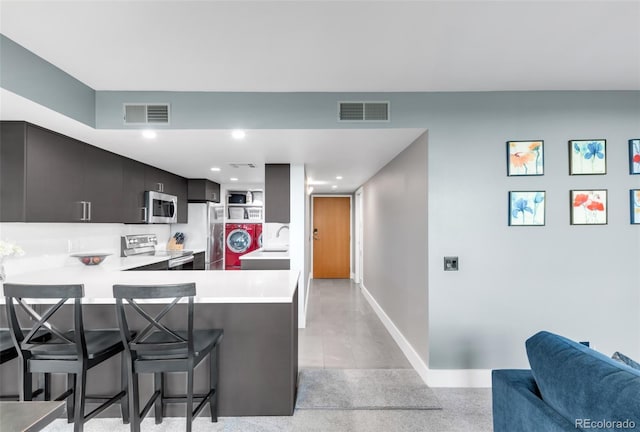 5955 E 10th Ave Unit 507, Denver, CO 80220 - kitchen featuring appliances with stainless steel finishes, a kitchen bar, light countertops, a peninsula, and washer / dryer