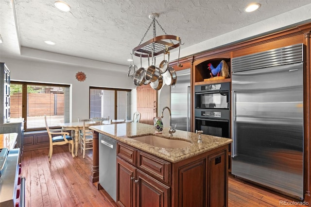 50 Albion St, Denver, CO 80220 - kitchen with appliances with stainless steel finishes, hardwood / wood-style floors, a textured ceiling, a center island with sink, and light stone countertops
