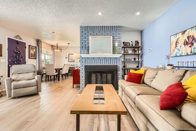living area with a fireplace, a textured ceiling, recessed lighting, and light wood-style floors