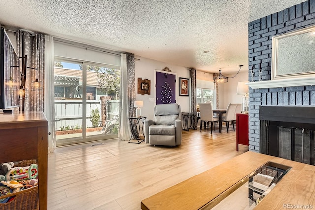 living area with a textured ceiling, visible vents, a chandelier, wood finished floors, and a fireplace