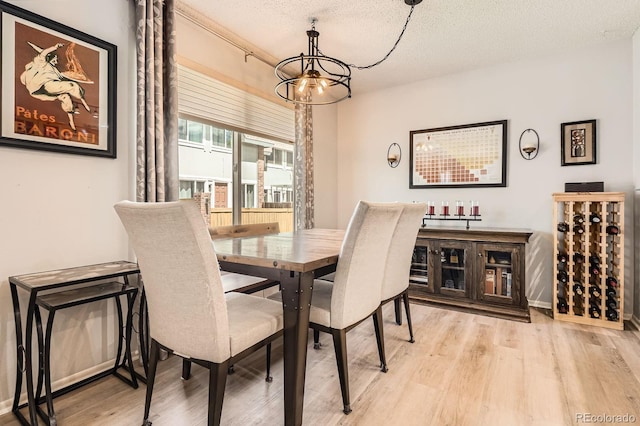 dining room featuring light wood finished floors, a textured ceiling, and an inviting chandelier