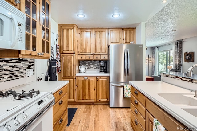 kitchen with a textured ceiling, light wood-type flooring, white appliances, light countertops, and decorative backsplash