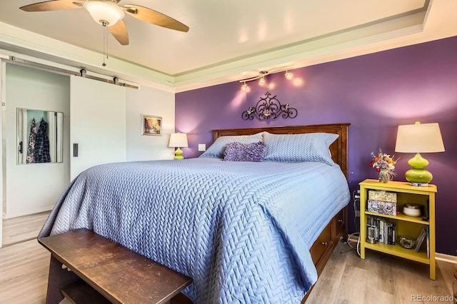 bedroom with wood finished floors, baseboards, a barn door, and a ceiling fan