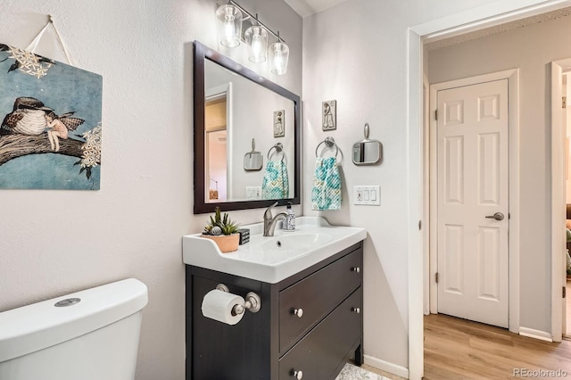 bathroom with toilet, baseboards, wood finished floors, and vanity