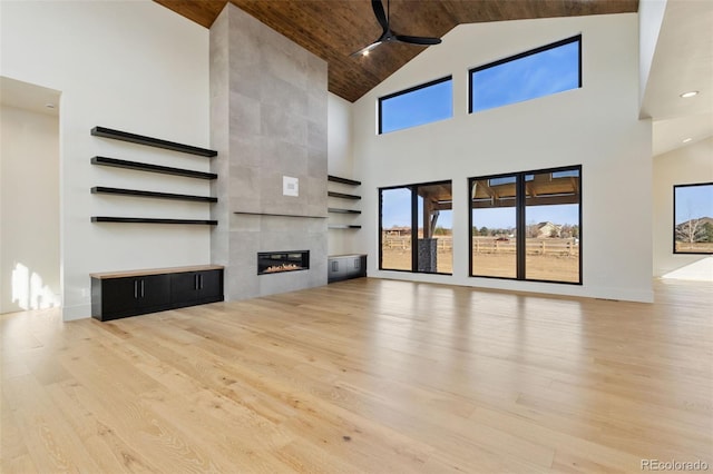 unfurnished living room with wood ceiling, ceiling fan, light hardwood / wood-style flooring, high vaulted ceiling, and a fireplace