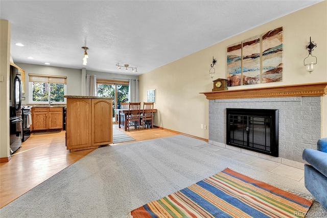 living area with a textured ceiling, light wood-style floors, baseboards, a brick fireplace, and recessed lighting
