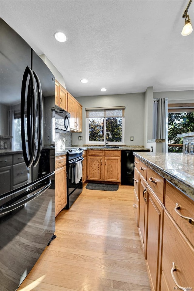 kitchen featuring a sink, tasteful backsplash, recessed lighting, light wood-style floors, and black appliances