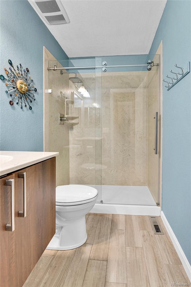 bathroom featuring a shower stall, toilet, vanity, and wood finished floors