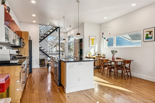 kitchen featuring light wood-style floors, stainless steel appliances, dark countertops, and a center island