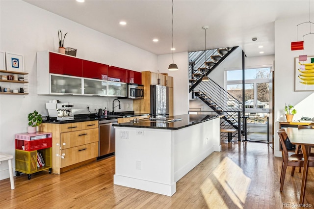 kitchen featuring a sink, a kitchen island, stainless steel appliances, light wood-style floors, and hanging light fixtures