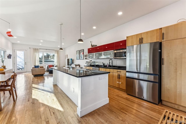 kitchen featuring dark countertops, a center island, light wood-type flooring, stainless steel appliances, and a sink