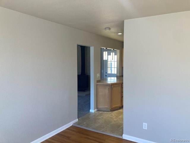 spare room with wood finished floors, a wood stove, and baseboards