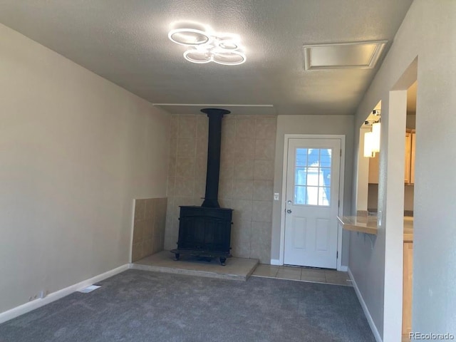 unfurnished living room with a textured ceiling, carpet floors, a wood stove, and baseboards