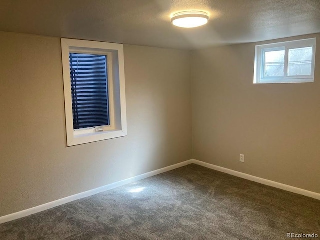 spare room with baseboards, dark carpet, and a textured ceiling