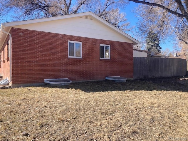 view of side of home featuring brick siding, fence, and a lawn