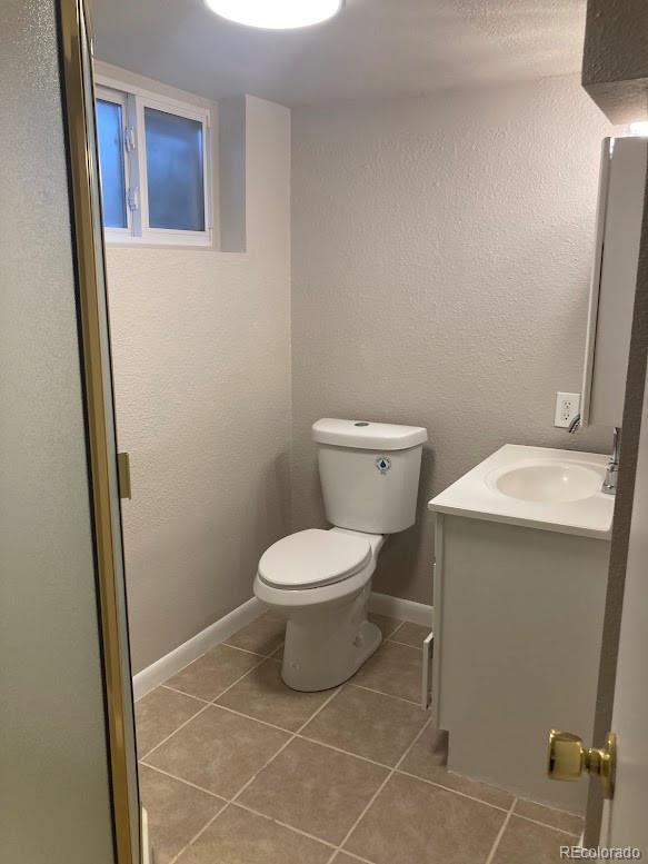 bathroom featuring a textured wall, toilet, vanity, baseboards, and tile patterned floors