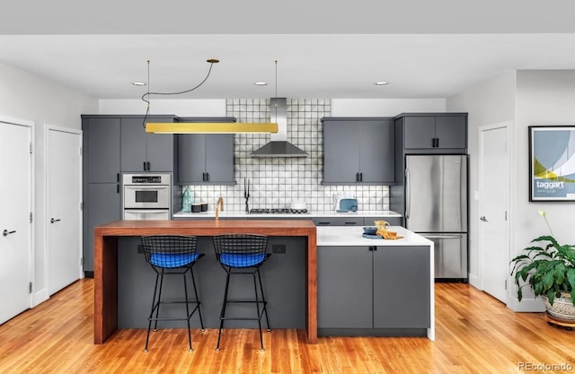 kitchen featuring a center island with sink, freestanding refrigerator, gray cabinetry, wall chimney range hood, and backsplash