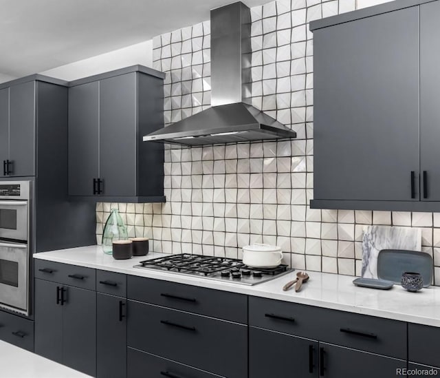 kitchen featuring wall chimney exhaust hood, tasteful backsplash, appliances with stainless steel finishes, and gray cabinetry