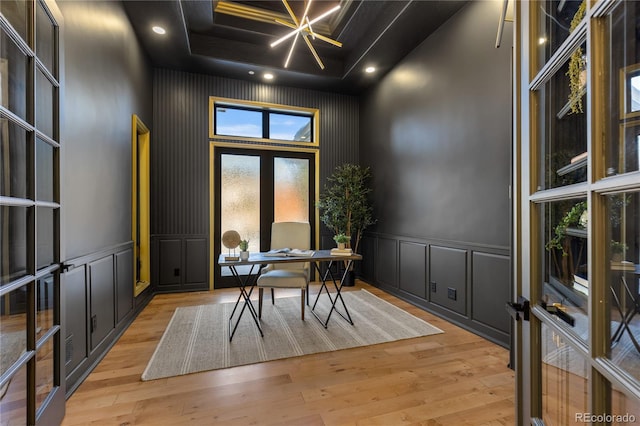 home office featuring a towering ceiling, french doors, light wood-type flooring, and a raised ceiling