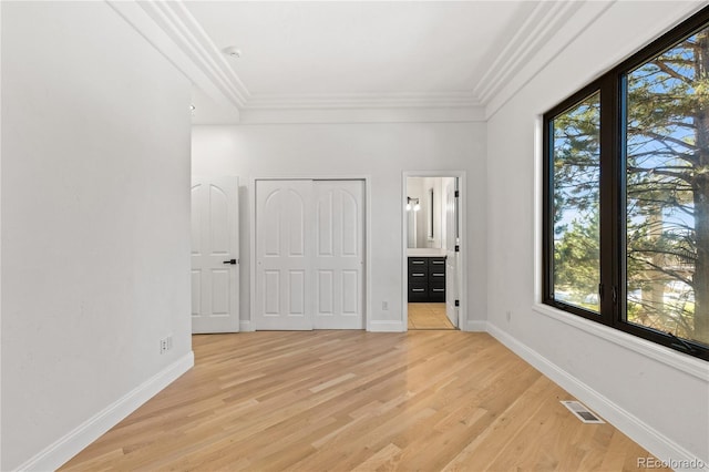 unfurnished bedroom featuring ensuite bathroom, a closet, ornamental molding, and light hardwood / wood-style flooring