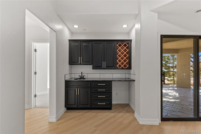 bar featuring sink, dark stone counters, and light wood-type flooring