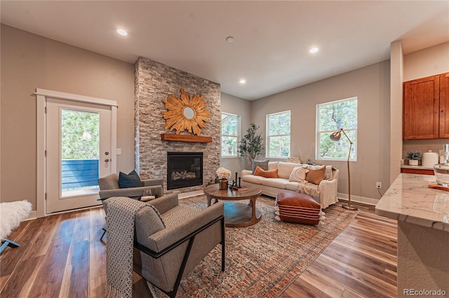 living room with a wealth of natural light, a stone fireplace, and hardwood / wood-style floors