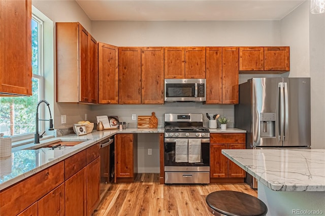 kitchen featuring stainless steel appliances, sink, light stone counters, and light hardwood / wood-style floors