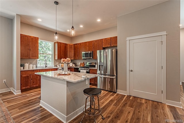 kitchen with a kitchen bar, sink, hanging light fixtures, appliances with stainless steel finishes, and a kitchen island