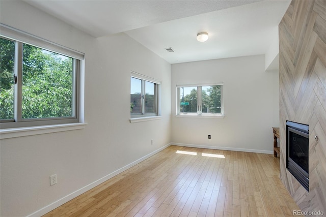 unfurnished living room featuring light wood finished floors, a fireplace, visible vents, and baseboards