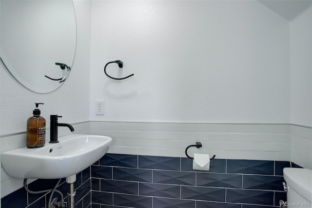 half bathroom with toilet, tile walls, a sink, and wainscoting