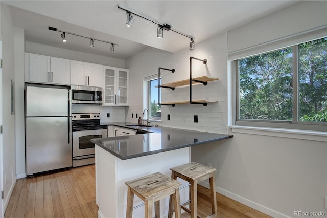 kitchen with decorative backsplash, appliances with stainless steel finishes, a sink, light wood-type flooring, and a peninsula