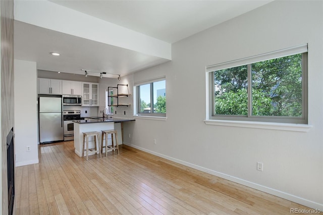 kitchen with light wood-style flooring, appliances with stainless steel finishes, glass insert cabinets, a peninsula, and baseboards