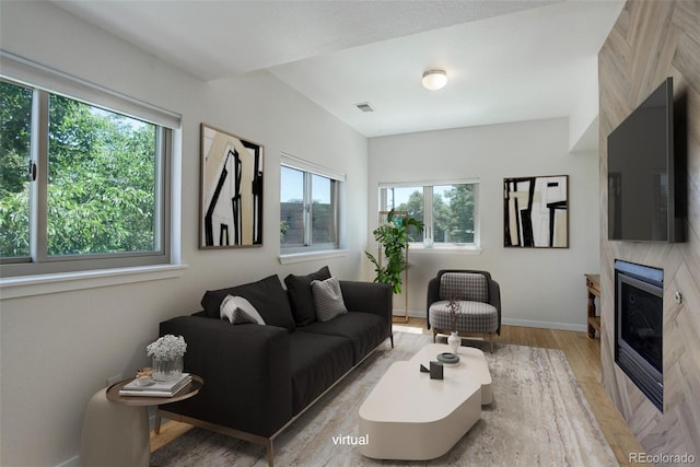 living room featuring a large fireplace, visible vents, wood finished floors, and a wealth of natural light