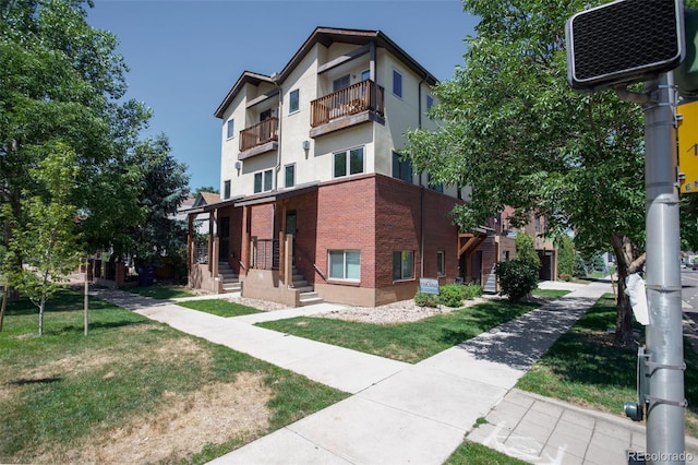 view of front of house with brick siding, a balcony, a front lawn, and stucco siding