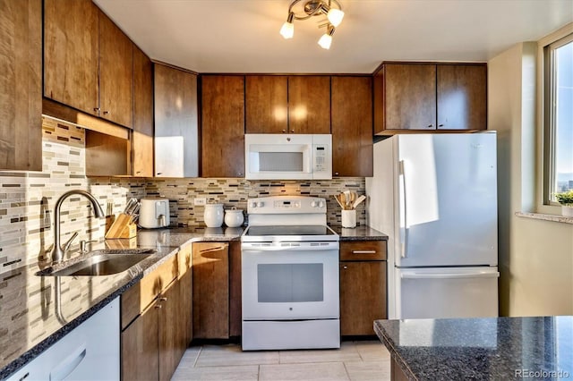 kitchen featuring white appliances, backsplash, a sink, and dark stone countertops