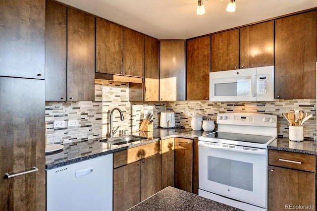 kitchen featuring decorative backsplash, brown cabinets, a sink, dark stone counters, and white appliances