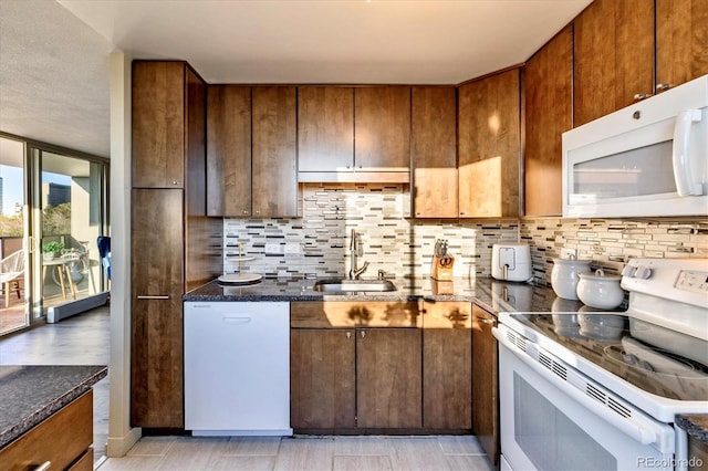 kitchen featuring a sink, dark stone counters, decorative backsplash, and white appliances