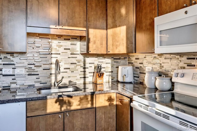 kitchen featuring a sink, dark stone counters, backsplash, and white appliances