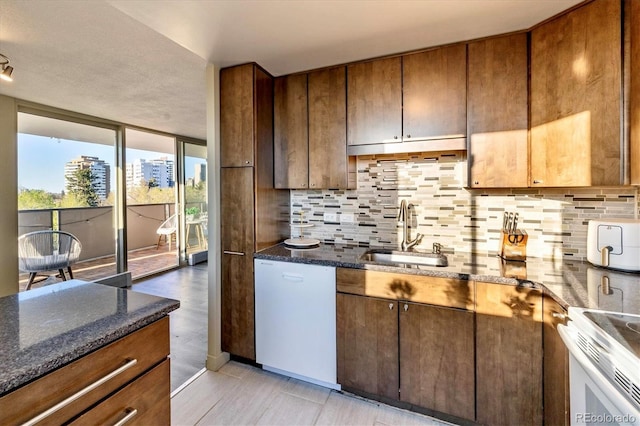 kitchen with white appliances, decorative backsplash, a sink, and dark stone countertops