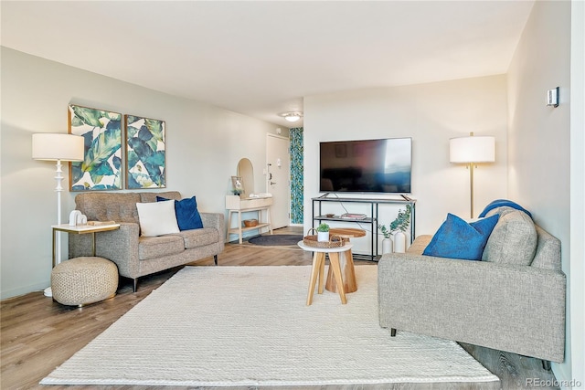 living area with baseboards, arched walkways, and wood finished floors