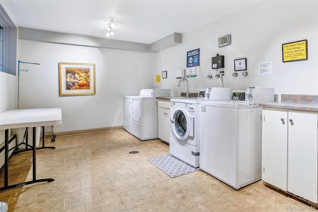 clothes washing area featuring baseboards, stone finish floor, cabinet space, and washer and clothes dryer