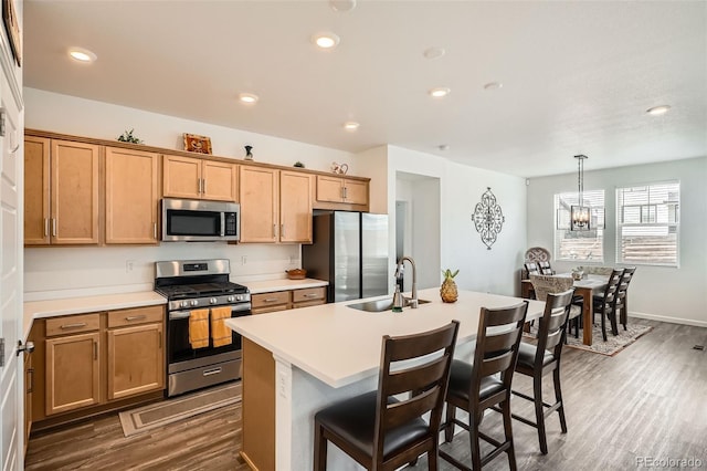 kitchen featuring appliances with stainless steel finishes, a sink, dark wood-style flooring, light countertops, and a kitchen breakfast bar