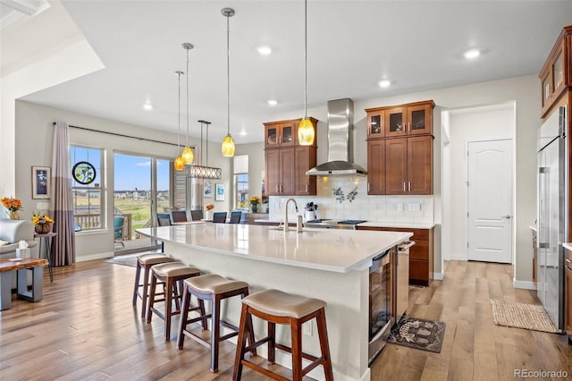 kitchen featuring wine cooler, decorative backsplash, hanging light fixtures, a center island with sink, and wall chimney exhaust hood