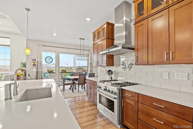 kitchen with sink, hanging light fixtures, stainless steel range, light hardwood / wood-style floors, and wall chimney exhaust hood