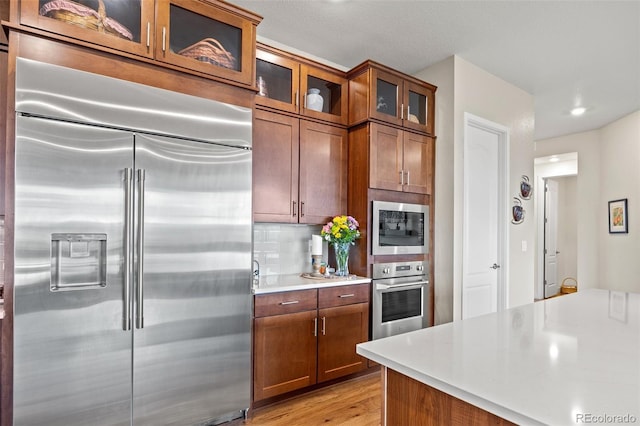 kitchen with tasteful backsplash, built in appliances, and light hardwood / wood-style flooring