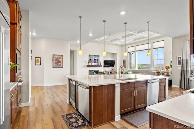 kitchen with coffered ceiling, an island with sink, sink, and decorative light fixtures