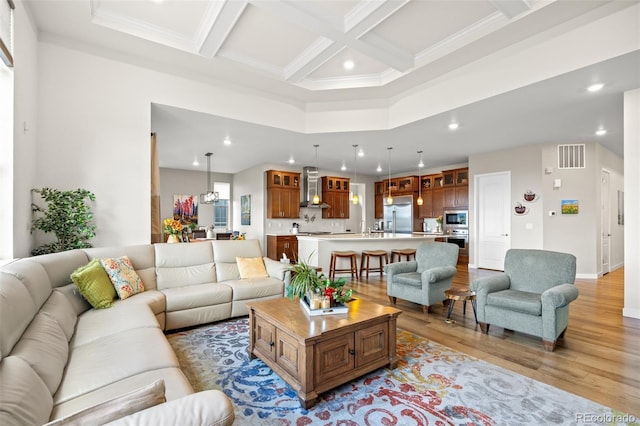 living room featuring beamed ceiling, a high ceiling, ornamental molding, coffered ceiling, and light wood-type flooring