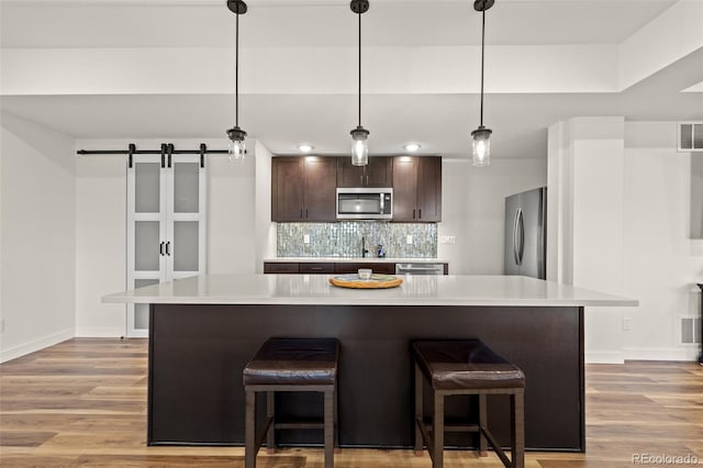 kitchen featuring dark brown cabinets, appliances with stainless steel finishes, decorative light fixtures, and a kitchen island