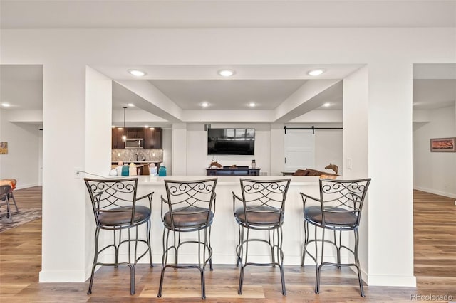 kitchen with a breakfast bar area, light hardwood / wood-style floors, a barn door, and kitchen peninsula